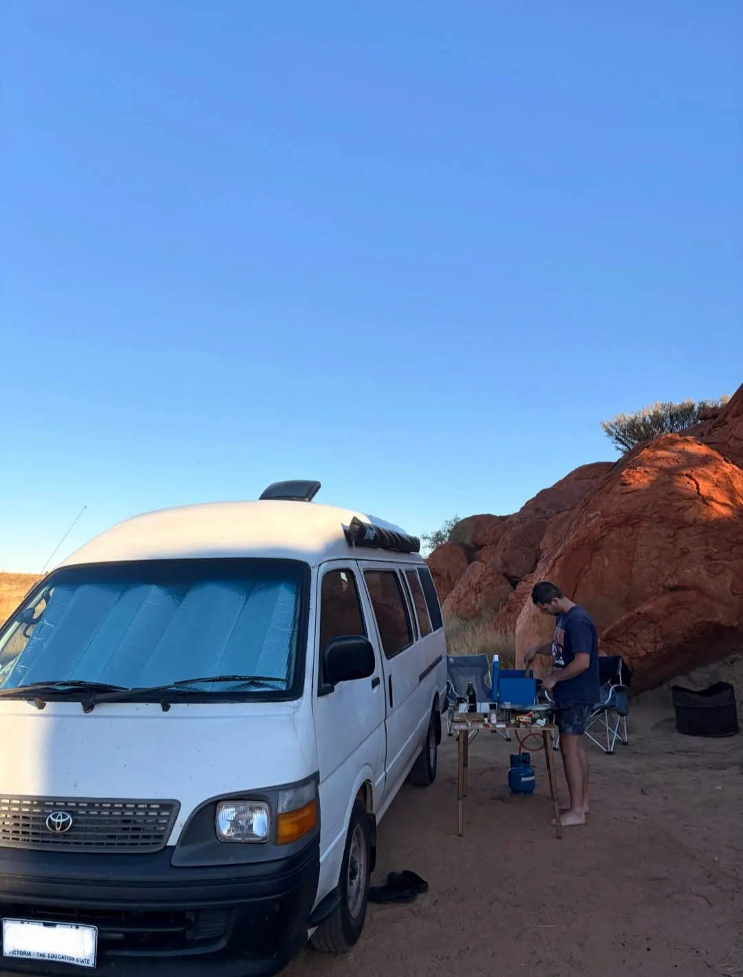 Hank parked by red boulders while a man cooks at the camp table