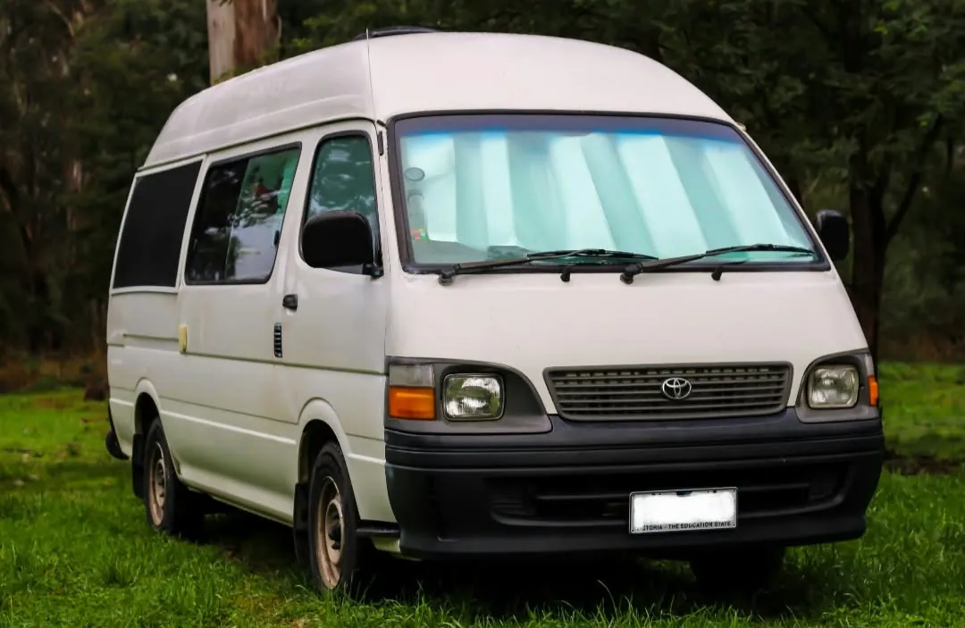 Hank, a white high-roof Toyota HiAce, parked on grass, front three-quarter view